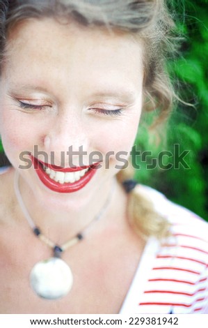 Close-up portrait of a happy young woman wearing red lipstick and natural eye makeup is laughing with her eyes closed.