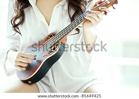 The Shot of a girl in the white shirt playing ukulele.