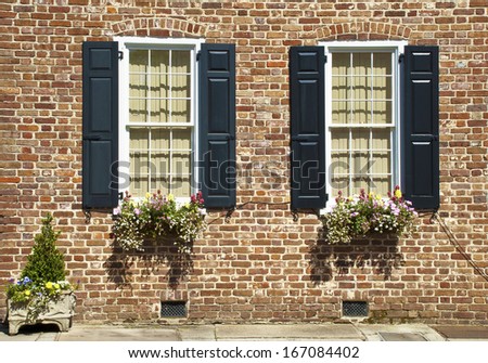 Shuttered windows decorated with flowers and plants in the brick wall of an eighteenth century house.