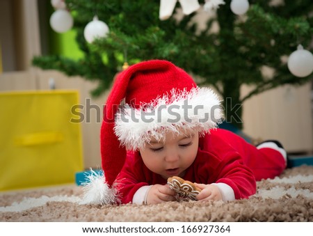 Happy baby dressed in Santa Claus hat and want to eat a cookie