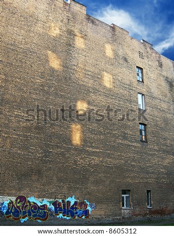 Windows virtual and real. Reflected sunlight on the old brick wall with graffiti in evening.