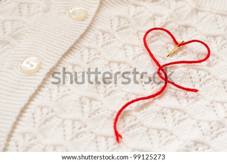The red thread in the needle in the shape of a heart on a white blouse