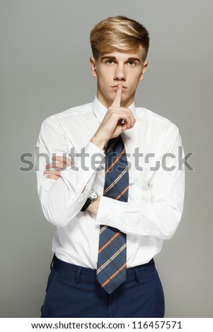 Business man with finger on lips asking for silence over gray background