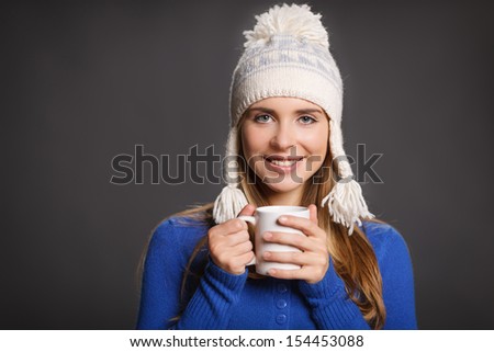 Winter woman wearing warm winter clothing: sweater and wool cap holding a snowflake, against gray background