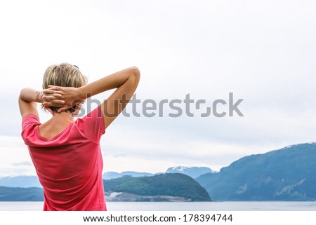 Back view of a woman enjoying a view at fjord with hands over head
