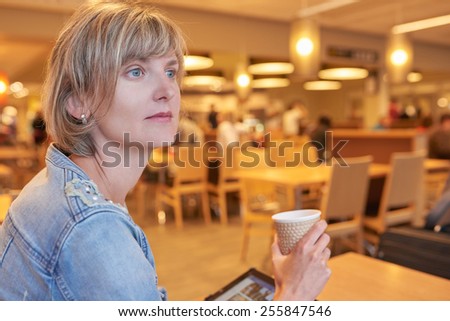 Closeup of a woman sitting in the cafe with cup of coffee and digital tablet thinking. Woman waiting for departure in airport cafe.