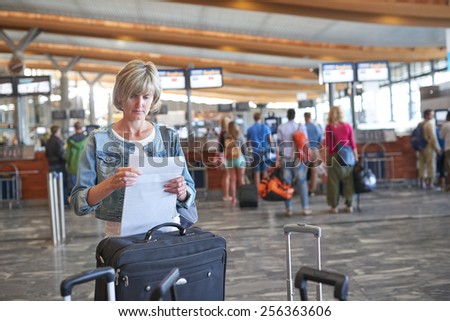 Woman standing with luggage in airport hall checking her e-tickets