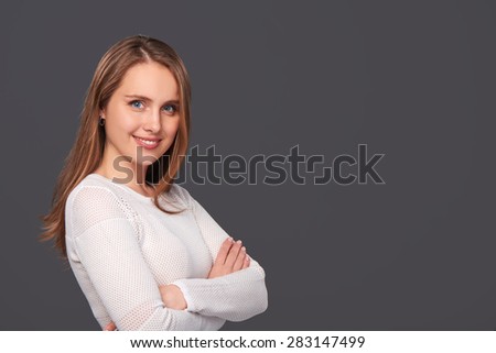 Portrait of smiling woman in white knitted dress standing with folded hands, over gray background