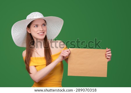 Summer style woman showing blank parcel - big envelope with copy space for text looking away, over green background