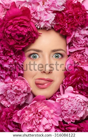 Closeup of beauty woman face with perfect skin and professional makeup in peony flowers pulling funny face