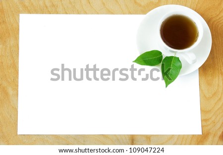 White blank with cup of  tea and fresh green leaves on wooden desk