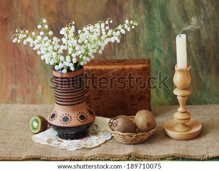 Still life with lily of the valley  bunch, candle, book  and fruits on artistic background