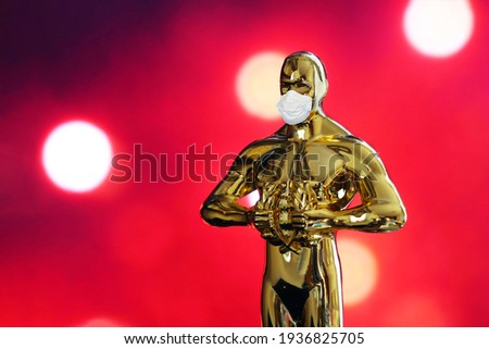 Hollywood Golden Oscar Academy award statue in medical mask on red background with copy space. Success and victory concept. Oscar ceremony in coronavirus time