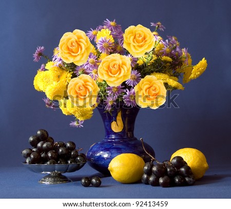 Huge bunch of autumn flowers and yellow roses, lemon and grapes on dark blue background
