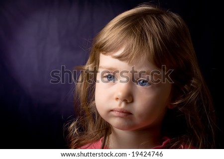 Portrait of beautiful little girl with blue eyes and curly hair on dark blue background. Focus on girl\'s right eye.