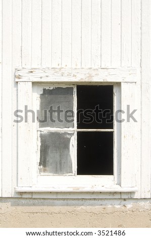 One of the windows of an old white barn is broken.