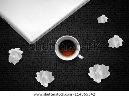 Crumpled colorful papers with laptop and coffee on black desktop.