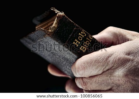 Aged man hands firmly holding and clinching an old and damaged antique Holy Bible Christian religious book during a religious prayer service in a protestant church