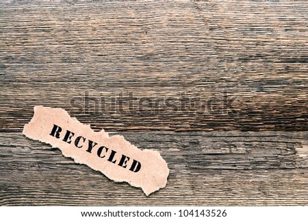 The ecological title word recycled printed on a piece of torn brown paper on reclaimed barnwood lumber background as metaphor for responsible environmental recycling and reuse of old natural material