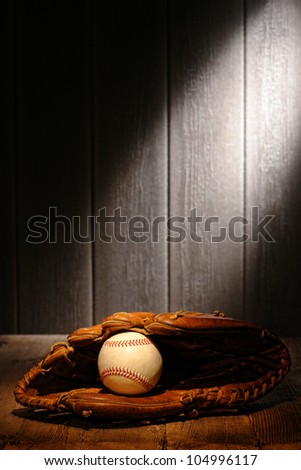 Vintage sport ball in an old baseball catcher leather glove on aged wood planks in an antique stadium dugout