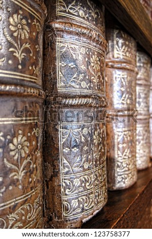 Old and worn leather cover bound books spine with aged gold leaf embossing on an antique wood library bookcase shelf