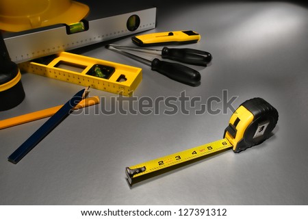 Self retracting yellow tape measure tool in inch measurement on metal surface with assorted trade tools at building construction work site