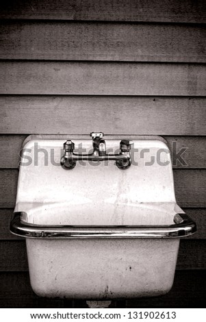 Vintage enamel washbasin utility tub sink with retro faucet mounted outside on an old house clapboard wall on a rural farm building