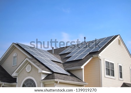 Renewable clean green energy saving efficient photovoltaic solar panels on multiple gable suburban house roof over blue sky