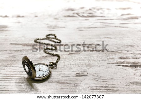 Vintage pocket watch and brass chain with scrolled detail and antique cardinal numbers keeping time on an old aged and weathered wood background