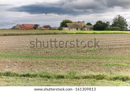 Old abandoned stone walls farm and farmhouse compound buildings with damaged roofs and structure behind agriculture farmland fields in the rural countryside of France