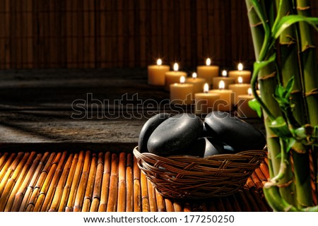 Smooth polished black hot massage stones in a basket with candles and bamboo stems in relaxing Zen inspired soothing atmosphere of wellness holistic spa for a natural well-being rejuvenation session