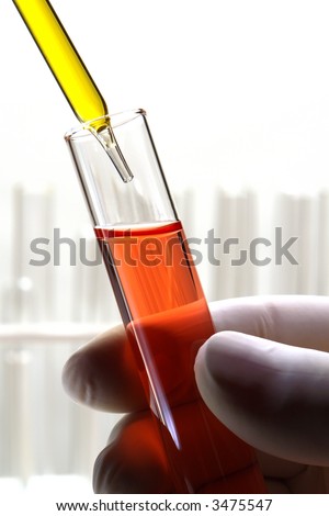 Scientist hand holding a laboratory glass test tube under a pipette filled with yellow liquid for an experiment in a science research lab