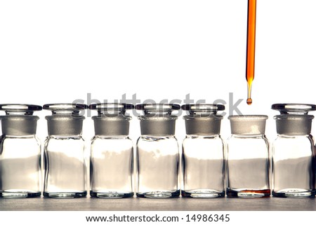 Laboratory pipette with drop of red liquid over chemical bottles in a science research lab