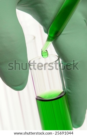 Scientist hand holding a laboratory glass test tube filled with green chemical solution under a pipette with drop of liquid for an experiment in a science research lab