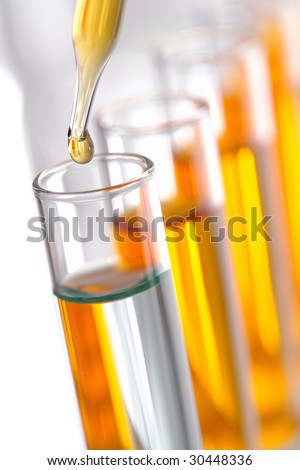 Laboratory pipette with drop of yellow liquid over glass test tubes for an experiment in a science research lab