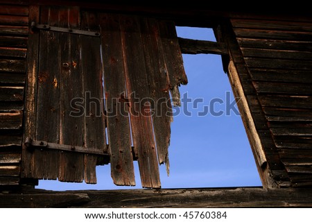 Damaged old wood barn door on an empty farm building over blue sky