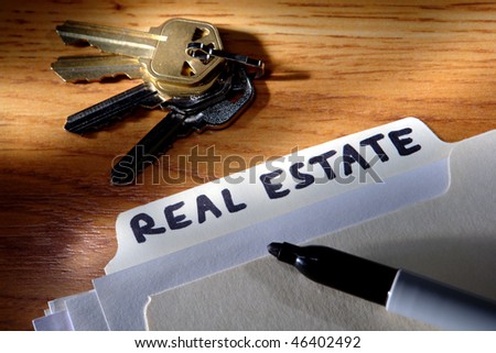 Real estate title words hand written with a marker on a file folder tab with papers and set of house keys on a desk
