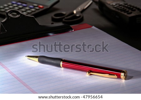 Ballpoint ink pen on a notepad ruled paper sheet attached to a clipboard on a desk