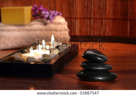 Polished black hot massage stone cairn with aromatherapy candles and towel for a Zen inspired wellness and relaxation session in a spa