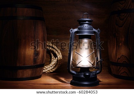 Old kerosene lantern burning with bright flame between wood barrels in a vintage country  barn warehouse