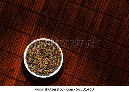 Dry aromatherapy lavender flower seeds in a ceramic bowl over a grunge bamboo mat in a spa
