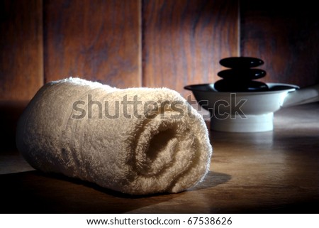 Soft white cotton towel and black polished hot massage stones cairn on a heater for a pampering relaxation treatment in a spa