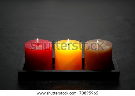 Elegant red yellow and green decorative marbleized pillar candles burning with a soft glow flame in a tray on sophisticated black