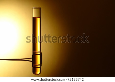 Laboratory glass test tube filled with yellow gold color liquid held in a specialized brass clamp during a scientific experiment in a science research lab