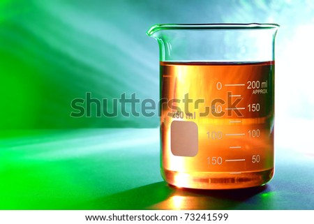 Graduated scientific glass beaker with amber orange chemical liquid over reflective background for a chemistry laboratory experiment in a science research lab