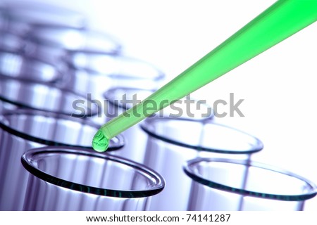 Laboratory pipette with drop of bright green liquid above empty chemical test tubes for a chemistry experiment in a science research lab