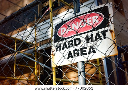 Danger hard hat area safety warning sign on a chain link fence at a house construction work site