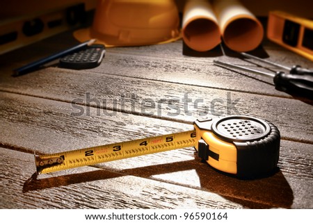 Self retracting yellow tape measure tool on wood boards with tools and plans at building construction work site