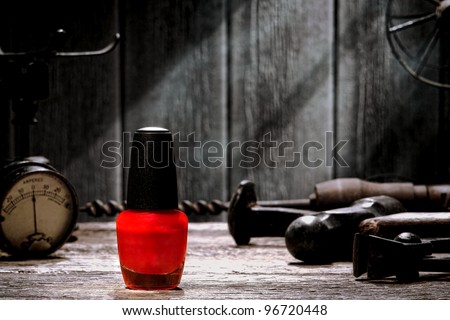Generic bottle of bright fashion color red nail liquid polish cosmetics on a vintage weathered wood workbench with antique industrial tools in an old grunge mechanic workshop
