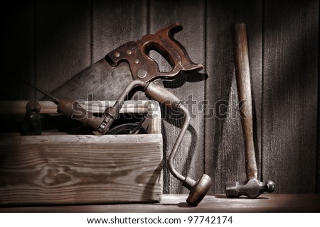 Old and used antique carpenter and handyman tools with drill and crosscut saw and hammer in an aged rustic wood toolbox in a vintage carpentry workshop